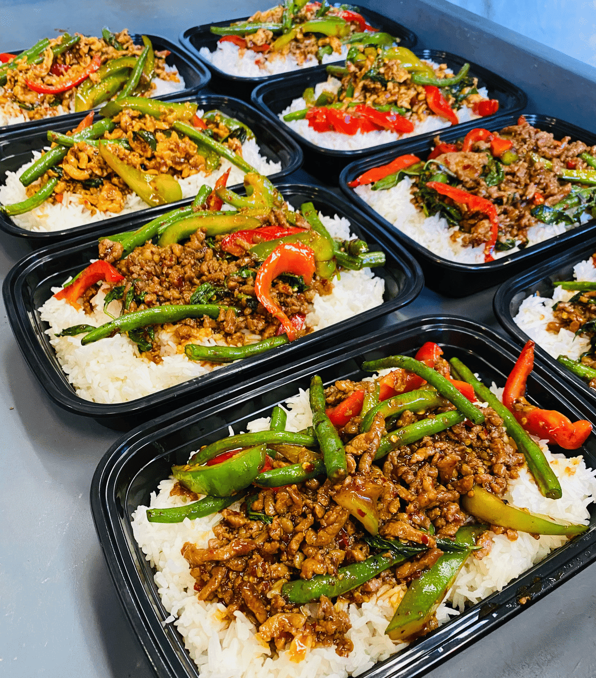 Rows of meal prep containers with rice, sautéed beef, and colorful vegetables.