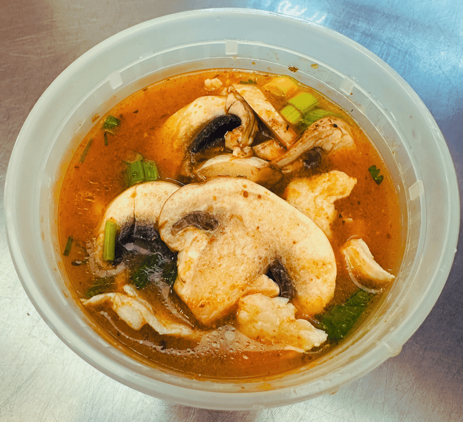 Spicy mushroom soup with herbs and seasoning in a clear plastic bowl.