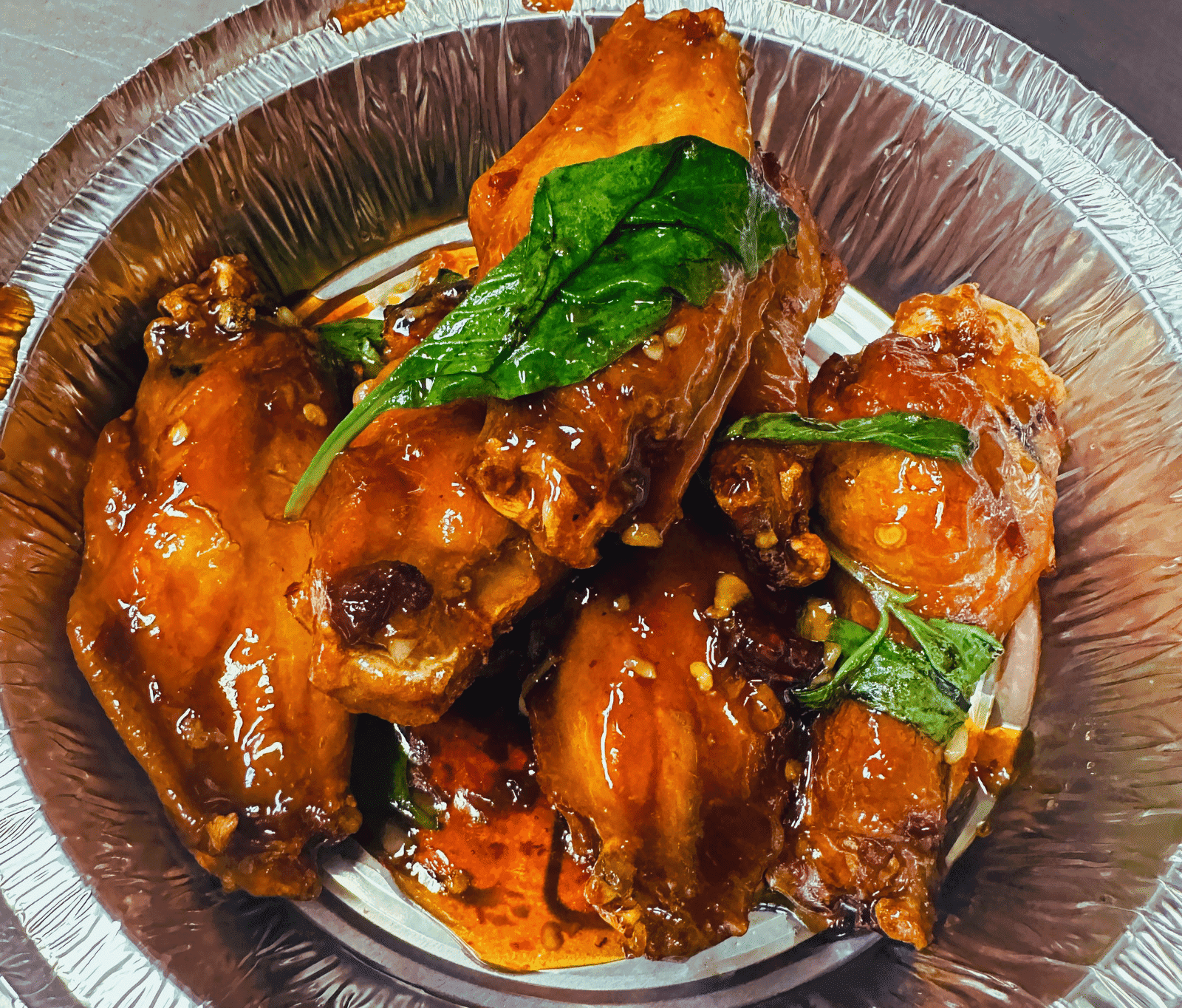 Chicken wings in spicy sauce garnished with fresh basil leaves in a round, metal dish.
