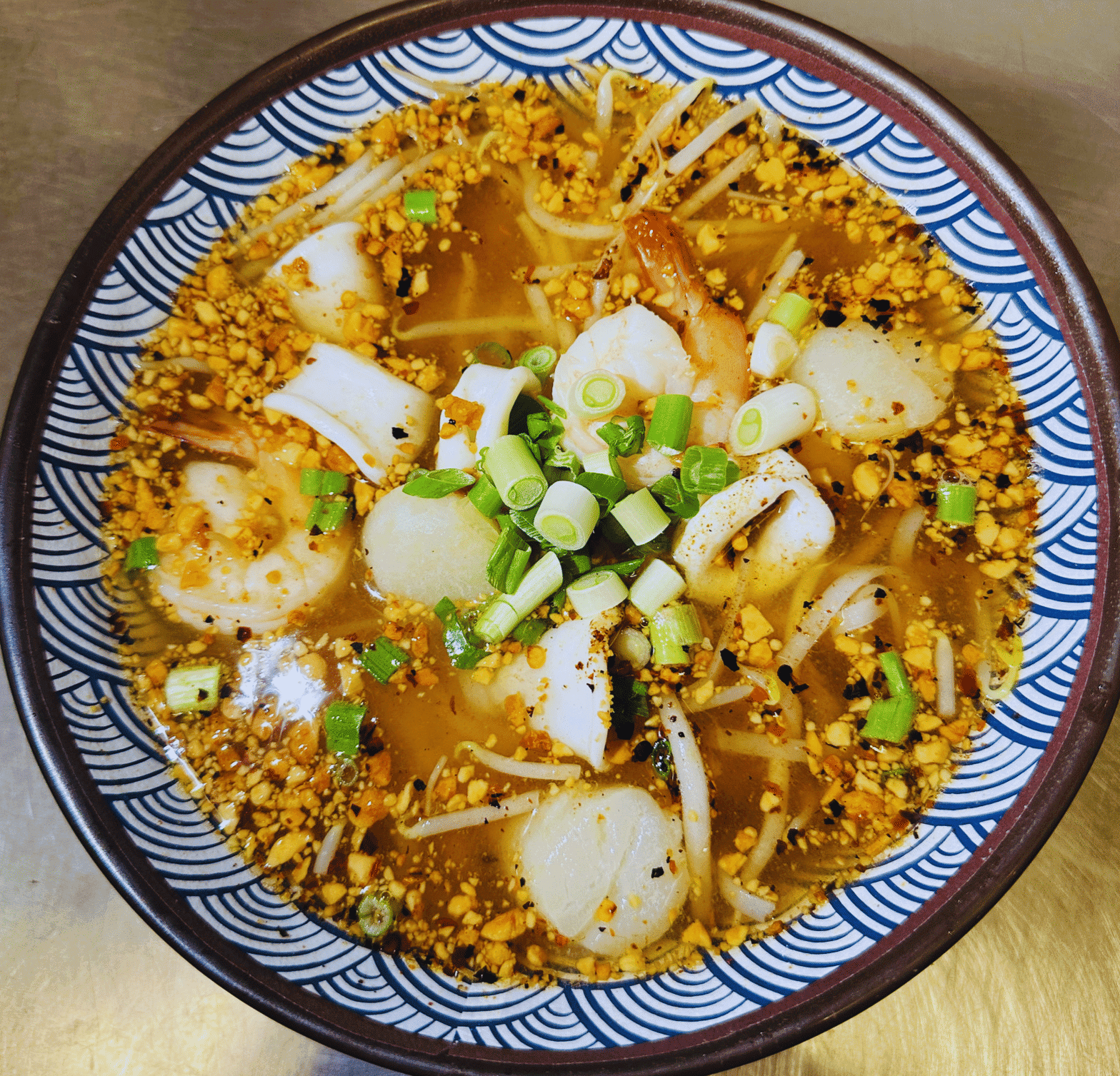 Bowl of spicy seafood ramen with shrimp, scallops, and green onions in a patterned bowl.
